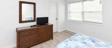 A bedroom with a bed, dresser, mirror, and window.