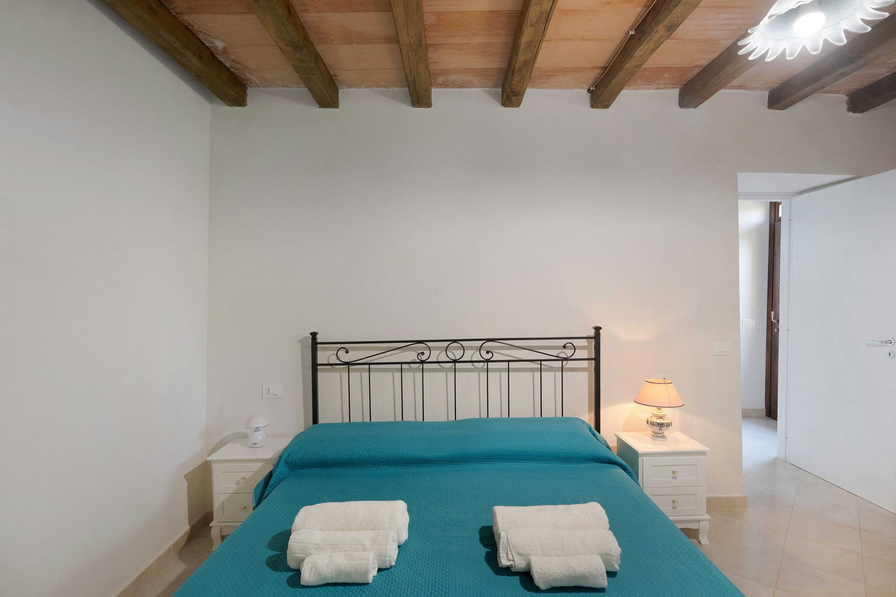 A bedroom with a bed, two bedside tables, a lamp, and a door leading to another room.