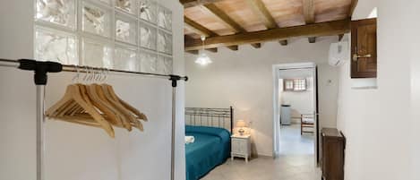 Un dormitorio con cama, mesita de noche, perchero y un pasillo que lleva a otra habitación.