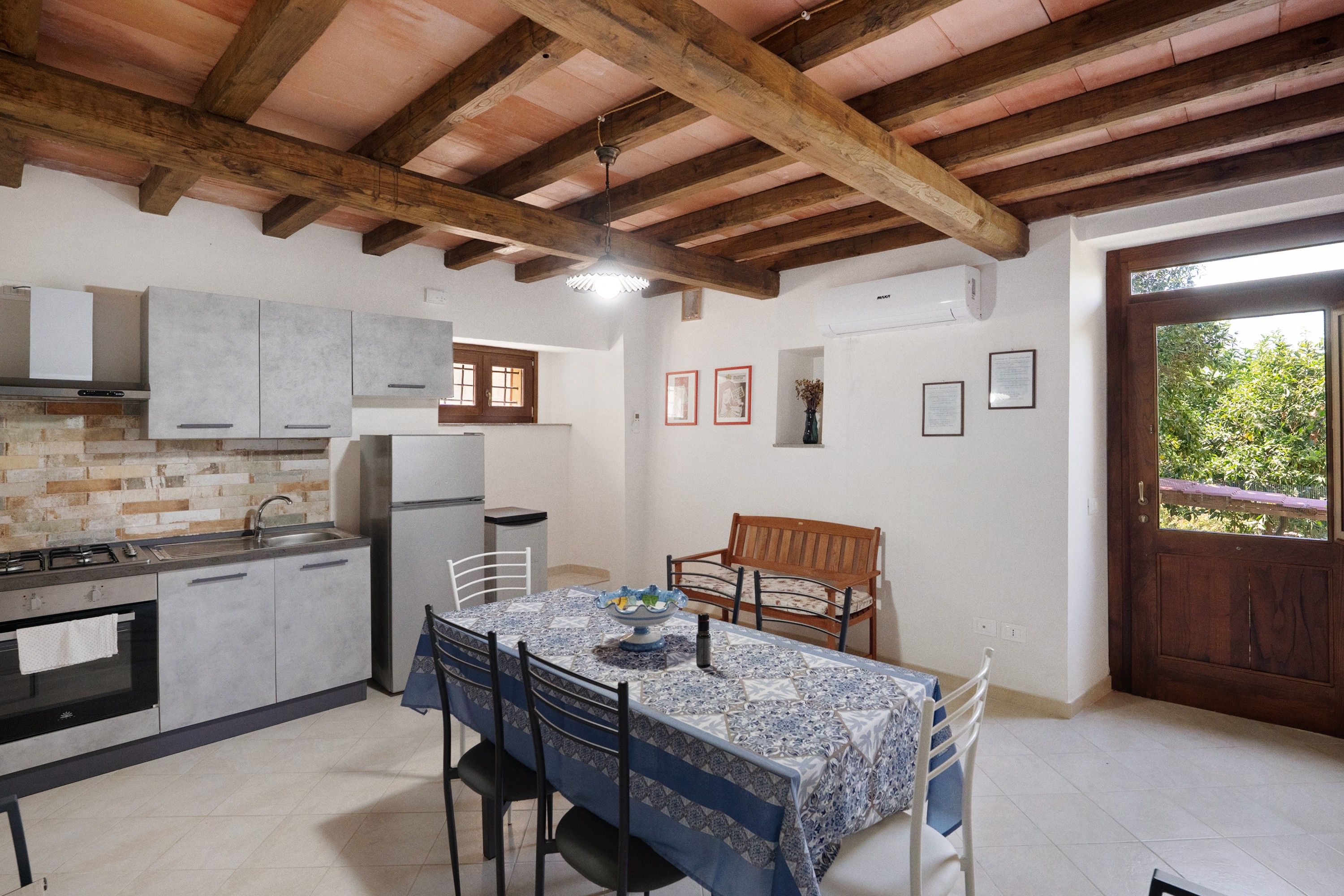 Une cuisine équipée d’appareils modernes, un coin repas avec une table dressée pour deux personnes, et une vue sur l’extérieur par une porte.