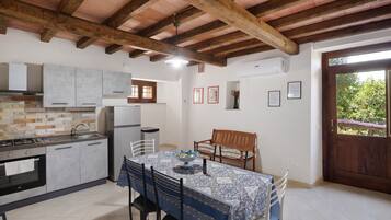 Une cuisine équipée d’appareils modernes, un coin repas avec une table dressée pour deux personnes, et une vue sur l’extérieur par une porte.