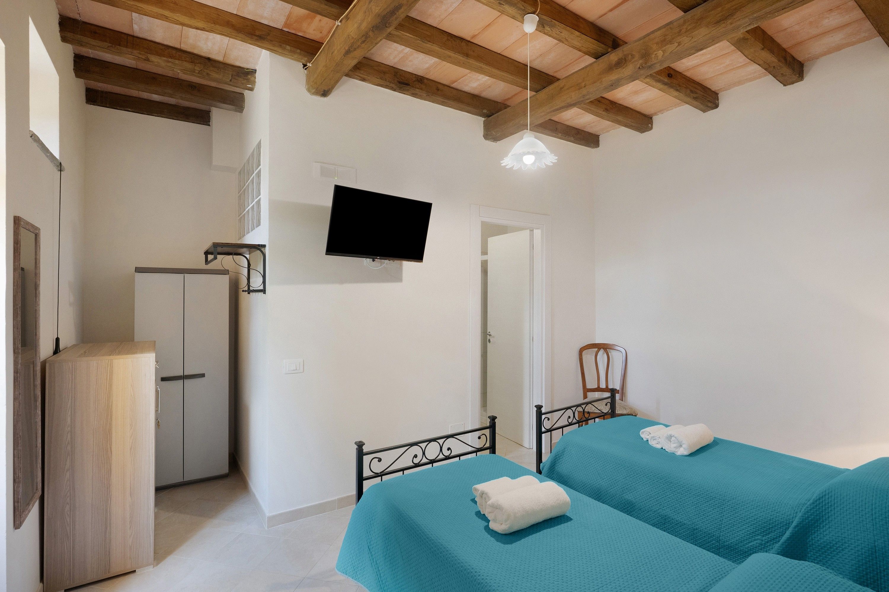 A bedroom with a bed, a wardrobe, a television, and a ceiling with wooden beams.