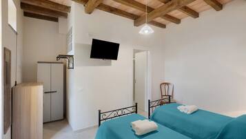 A bedroom with a bed, a wardrobe, a television, and a ceiling with wooden beams.