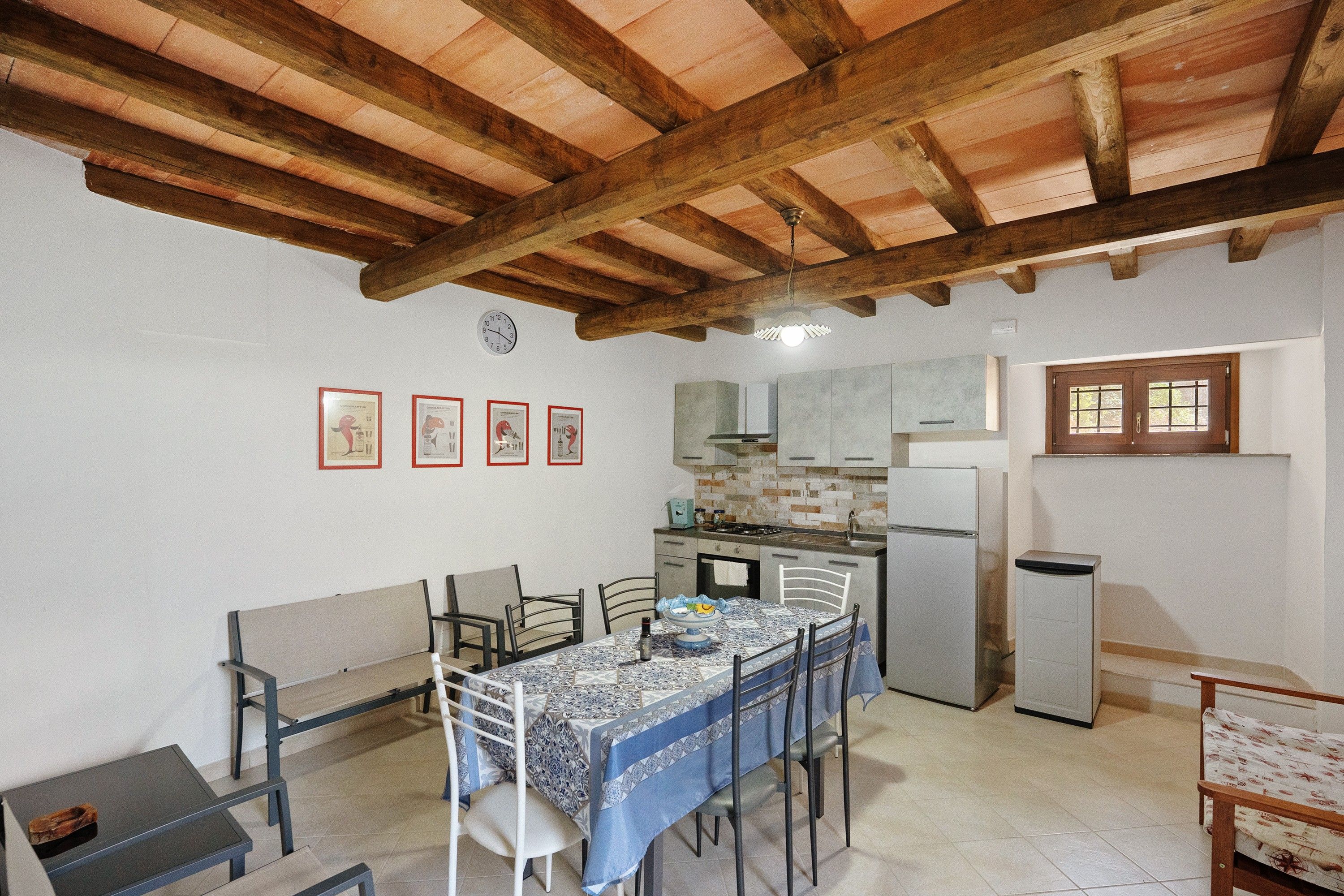 A compact kitchen with a dining area, featuring a tiled backsplash, wooden beams, and a refrigerator.