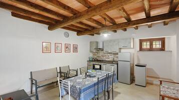 A compact kitchen with a dining area, featuring a tiled backsplash, wooden beams, and a refrigerator.