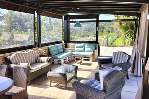 Un espacio de estar techado al aire libre con mobiliario de mimbre y vistas a un jardín.