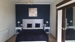 Een slaapkamer met een bed, twee nachtkastjes, een kroonluchter, een schilderij en een deur.