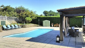 Een zwembad met ligbedden, een pergola en een tuinhuisje.