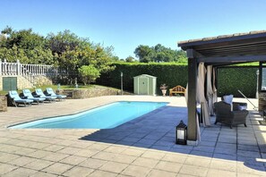 Une piscine avec des chaises longues, une pergola et un petit abri de jardin.