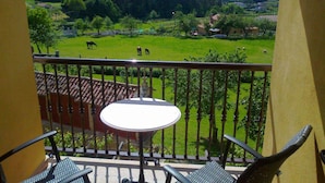 A balcony with a table and chairs, offering a view of a green field with grazing animals.