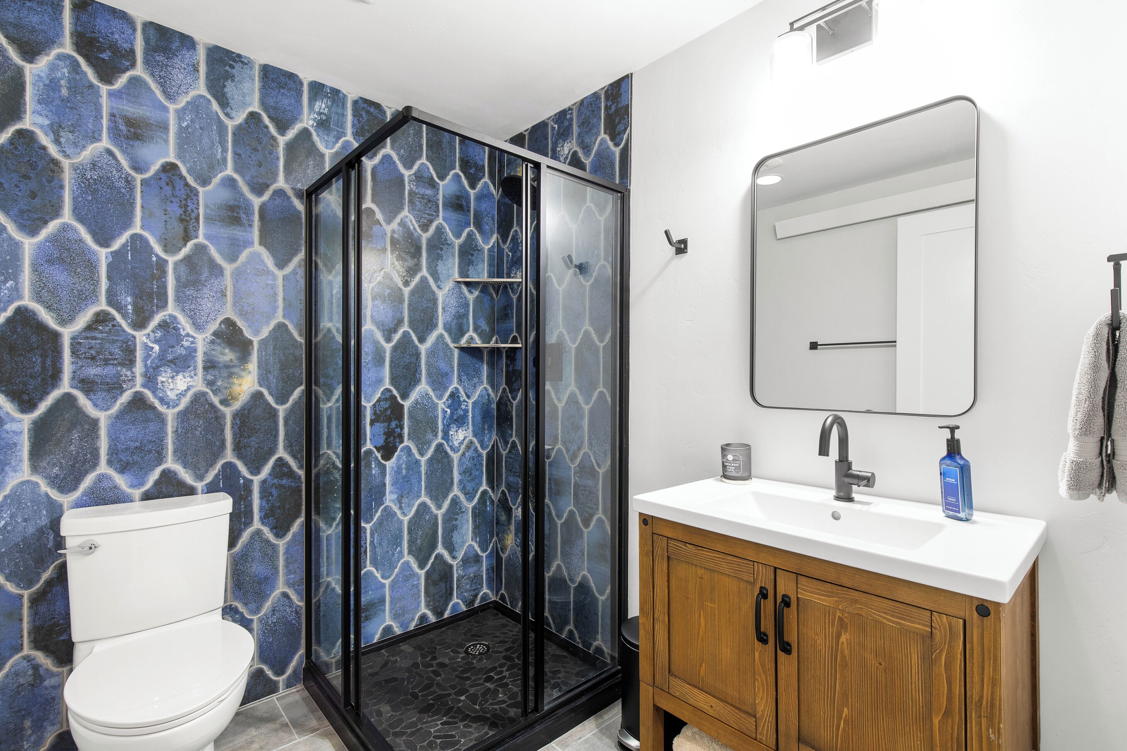 A bathroom with a shower enclosure, a toilet, a sink with a mirror, and wooden cabinets.