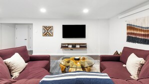 Ett modernt vardagsrum med två soffor, ett soffbord i glas, en platt-TV som är monterad på väggen och en dekorativ väggdekoration.