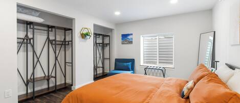 Um quarto com uma cama, uma cadeira, uma janela com persianas e um armário com uma estante de metal.