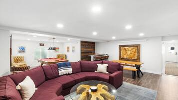 Ein modernes Wohnzimmer mit einer Eckcouch, einem Billardtisch und einem Essbereich mit Holztisch und Stühlen.