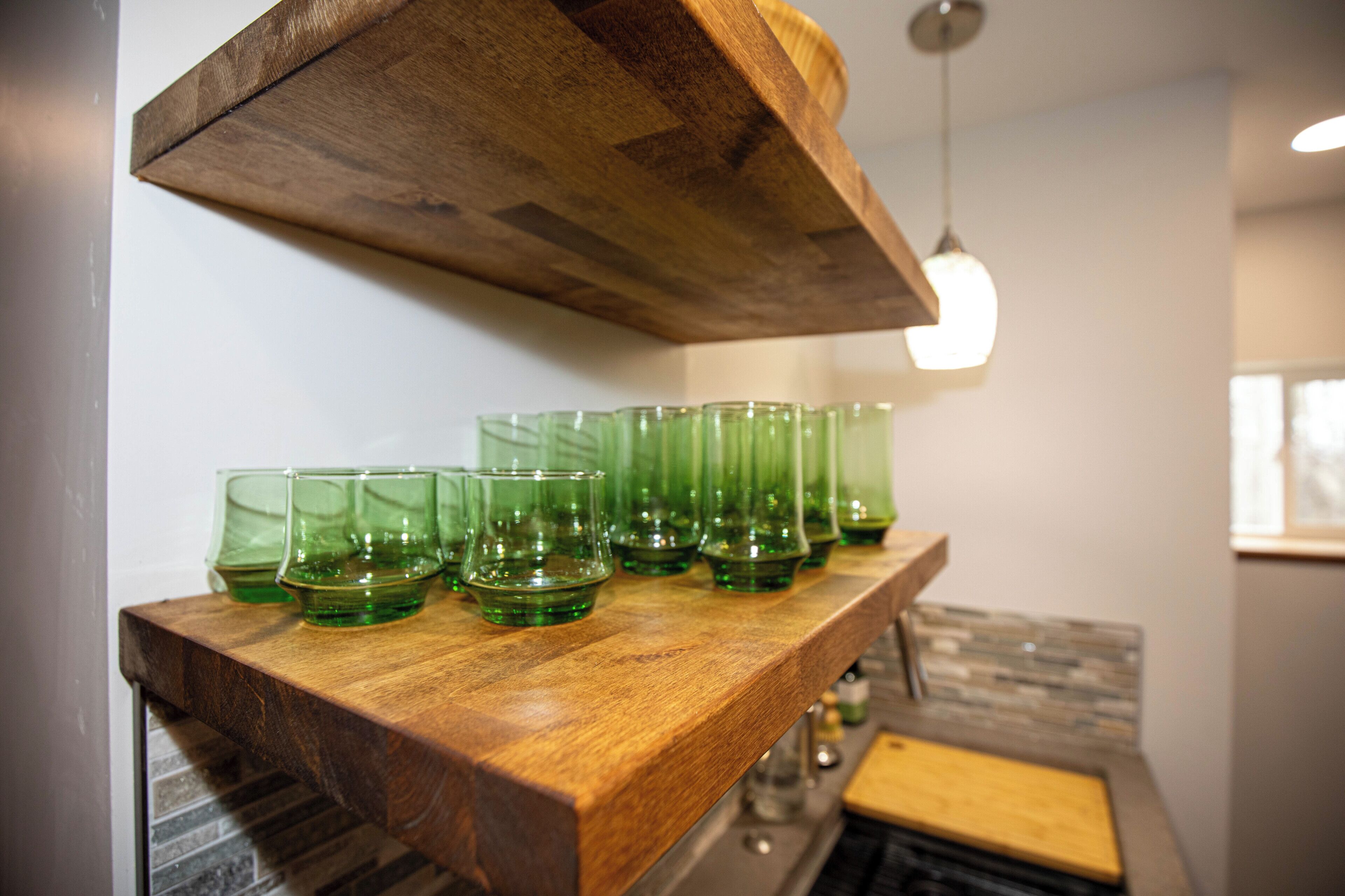 En køkkenbordplade med en træhylde, der holder flere grønne glas.'