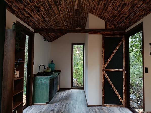 Ein Zimmer mit Holzboden, einem grünen Schrank, einer schwarzen Tür und Blick auf Grünfläche.