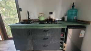 Una cocina equipada con estufa a gas, hervidor de agua, dispensador de agua y refrigerador.