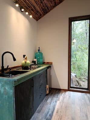 Eine Küche mit Einbauherd, einem großen Wasserspender und Blick auf einen Wald durch ein Fenster.