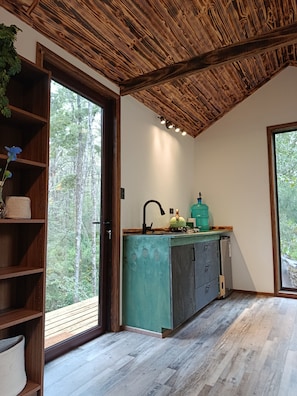Eine Küche mit Holzbalkendecke, einem großen Fenster und Blick auf den Wald.