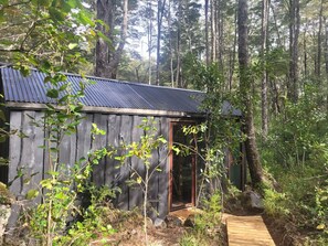 A rustic cabin with a metal roof, surrounded by dense forest. - Komorebi Lodge | River, forest, clay tub, breakfast, transportation. All-inclusive (Huililco)