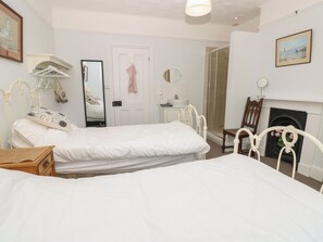 Ein Schlafzimmer mit zwei Einzelbetten, einem Nachttisch, einem Spiegel, einer Kommode, einem Sessel und einem Kamin.