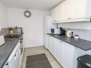 Eine kleine Küche mit weißen Schränken, einer Mikrowelle, einem Toaster und einer Kaffeemaschine auf der Arbeitsplatte.