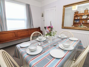 A dining room with a striped tablecloth, white plates, and a vase of flowers. - Bay Tree Cottage (Shanklin)