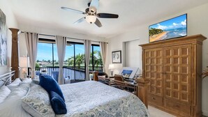 Ein Schlafzimmer mit einem Bett, einem Schreibtisch, einem Fernseher und Blick auf einen Strand.