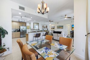 A modern kitchen with a central island, dining area with a glass table and chairs, and a living room with a sofa and TV. - Beautiful Marina views (Cape Coral)