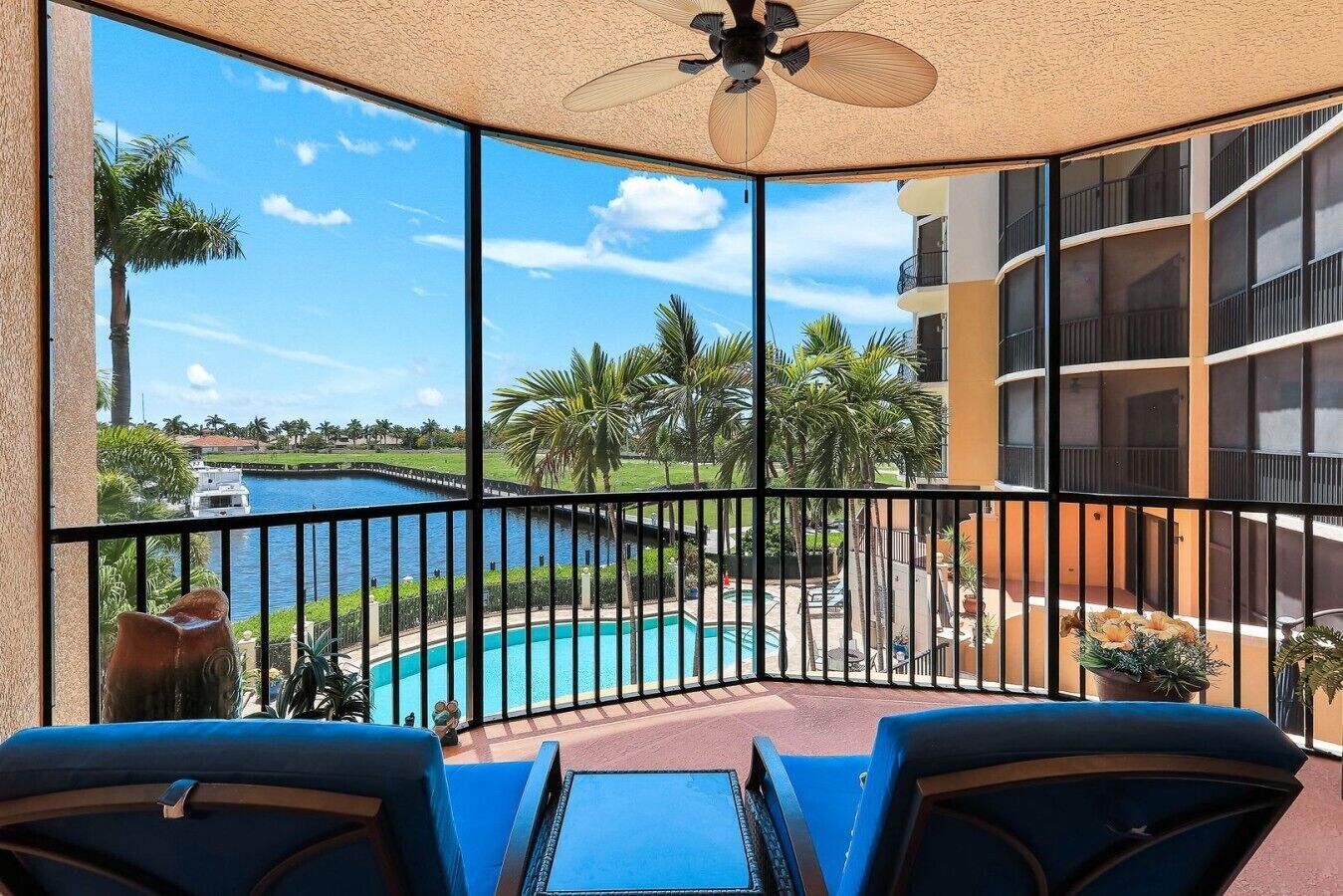 A balcony with a view of a swimming pool, palm trees, and a distant body of water.
