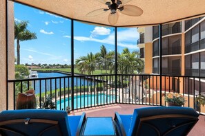 A balcony with a view of a swimming pool, palm trees, and a distant body of water. - Beautiful Marina views (Cape Coral)