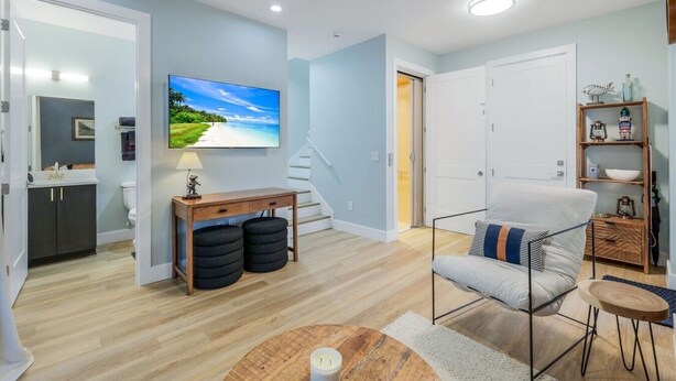 Una sala de estar moderna con un televisor de pantalla plana, una mesa de centro de madera, un sillón cómodo y una escalera que lleva a otra habitación.