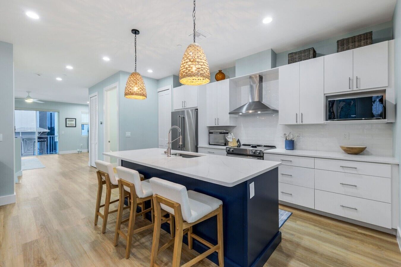 Une cuisine moderne dotée d’un îlot central, de meubles blancs, d’appareils électroménagers en acier inoxydable et de luminaires suspendus.