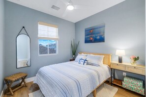 Une chambre à coucher avec un lit, une table de chevet, une lampe, un miroir, une fenêtre et un tableau accroché au mur.