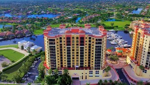 Un hotel moderno de gran altura con varios balcones, un puerto deportivo y vista a una zona residencial.