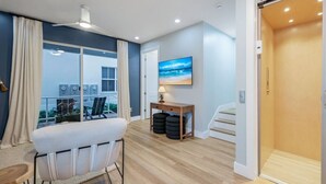 Una habitación moderna con balcón, un sofá, una mesa con lámpara y televisión en la pared.