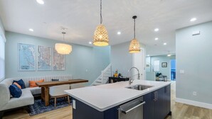 Una cocina moderna con una isla central, iluminación colgante y un comedor con sofá y mesa.