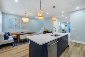 A modern kitchen with a central island, pendant lighting, and a dining area with a sofa and table. - Townhouse in Cape Harbour- Sleeps 8 (Cape Coral)
