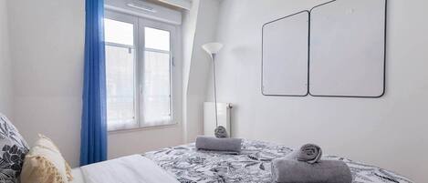 A bedroom with a bed, two wall-mounted mirrors, a window with blue curtains, and a radiator.
