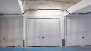 Een parkeergarage met drie gesloten garagedeuren, een blauwe veiligheidslijn en pijlen op de vloer.