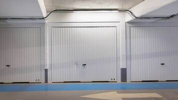 A parking garage with three closed garage doors, a blue safety line, and directional arrows on the floor.