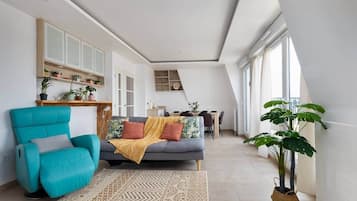 A modern living room with a sofa, armchair, and a dining area in the background.