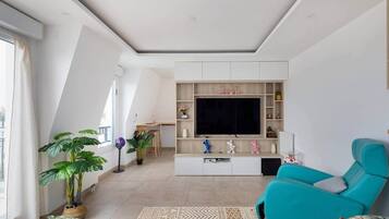 A modern living room with a large TV, a teal sofa, and a dining area with a table and chairs.