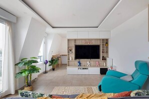 A modern living room with a large TV, a teal sofa, and a dining area with a table and chairs. - Clamart 92 • Paris • Béclère Hospital • Tram T6/T10 (Clamart)