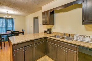 Una cocina con gabinetes de madera oscura, encimera de granito, lavamanos doble y cafetera.