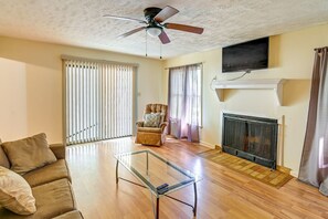 Ein Wohnzimmer mit Glastisch, Sofa, Sessel, Kamin und Deckenventilator.