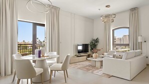 A modern living room with a dining area, a sofa, a TV, and large windows with city views. - Silkhaus Premium 1BR Stay in Yas Golf Collection (Abu Dhabi)
