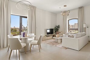 A modern living room with a dining area, a sofa, a TV, and large windows with city views. - Silkhaus Premium 1BR Stay in Yas Golf Collection (Abu Dhabi)