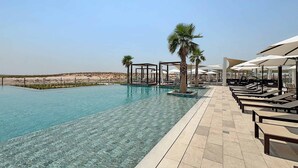 A pool with clear water, lounge chairs, umbrellas, and palm trees. - Silkhaus Premium 1BR Stay in Yas Golf Collection (Abu Dhabi)