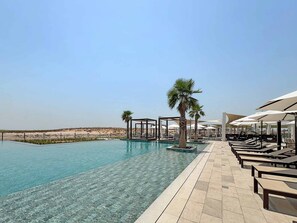A pool with clear water, lounge chairs, umbrellas, and palm trees. - Silkhaus Premium 1BR Stay in Yas Golf Collection (Abu Dhabi)